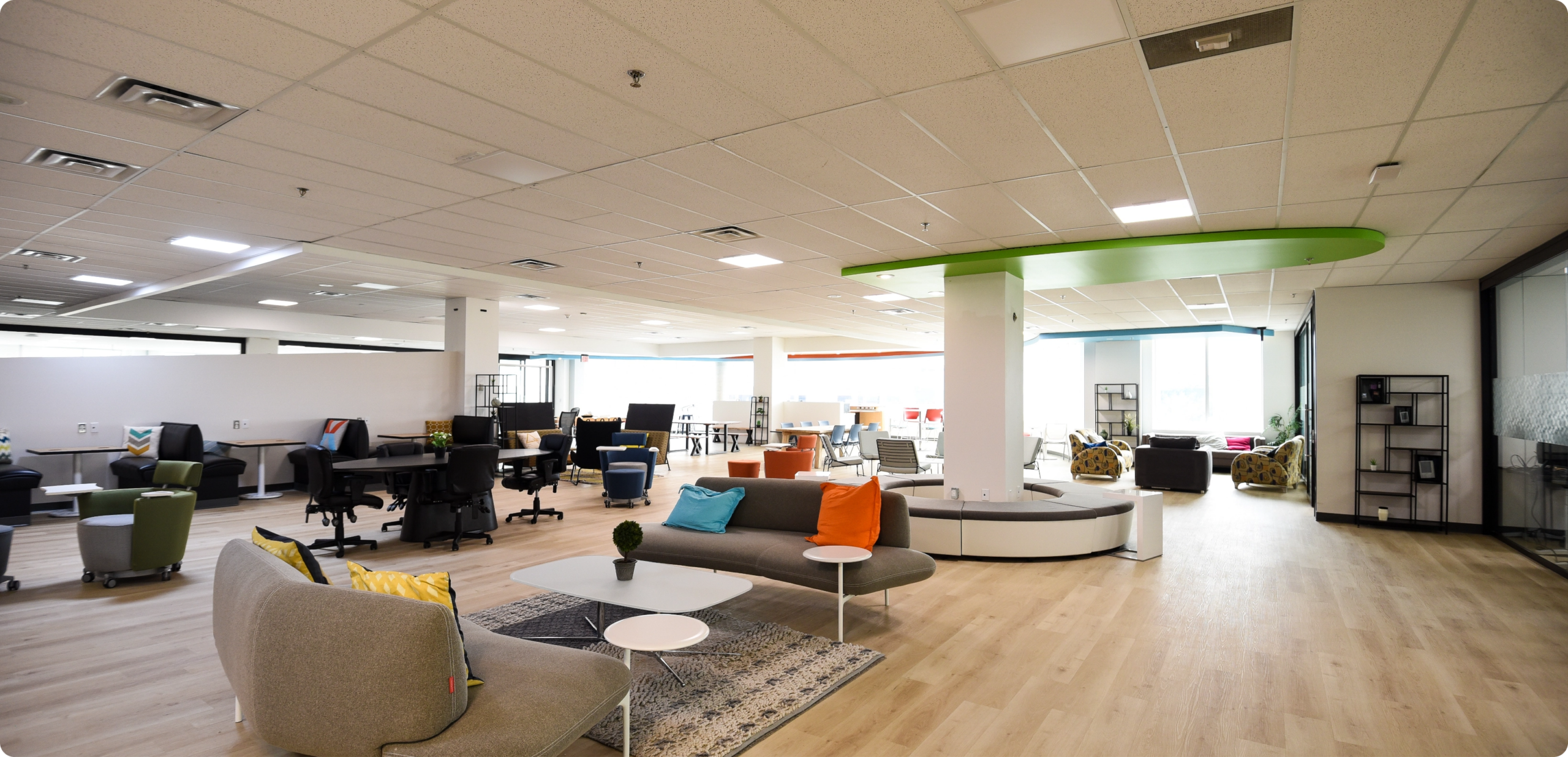 Bright, modern office: open workspaces, lounge, desks, light wood, green ceiling.