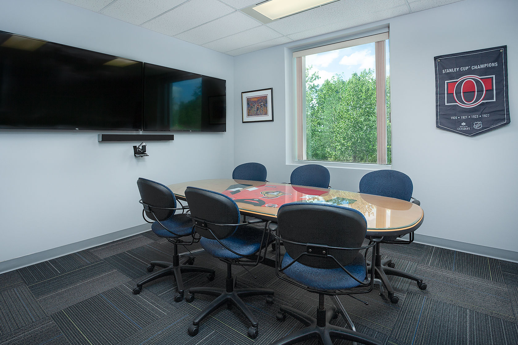 Small, modern meeting room with a hockey-themed table and a "Stanley Cup Champions" banner.