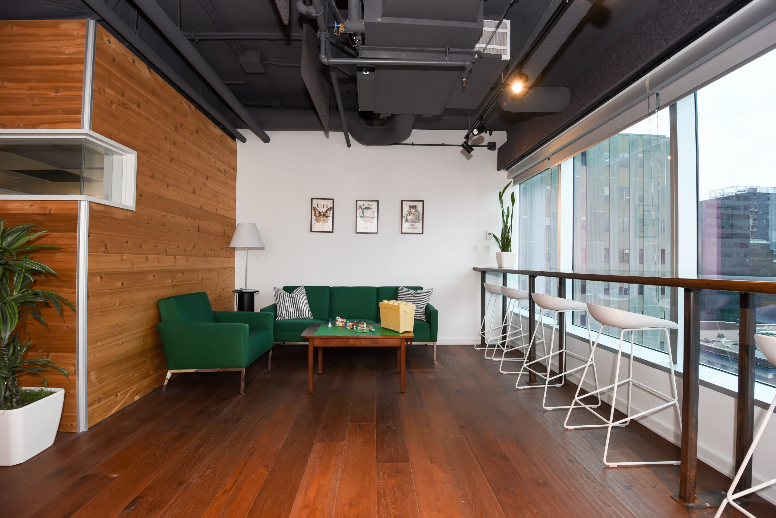 Contemporary office relaxation area with a green sofa, armchairs, and city views.