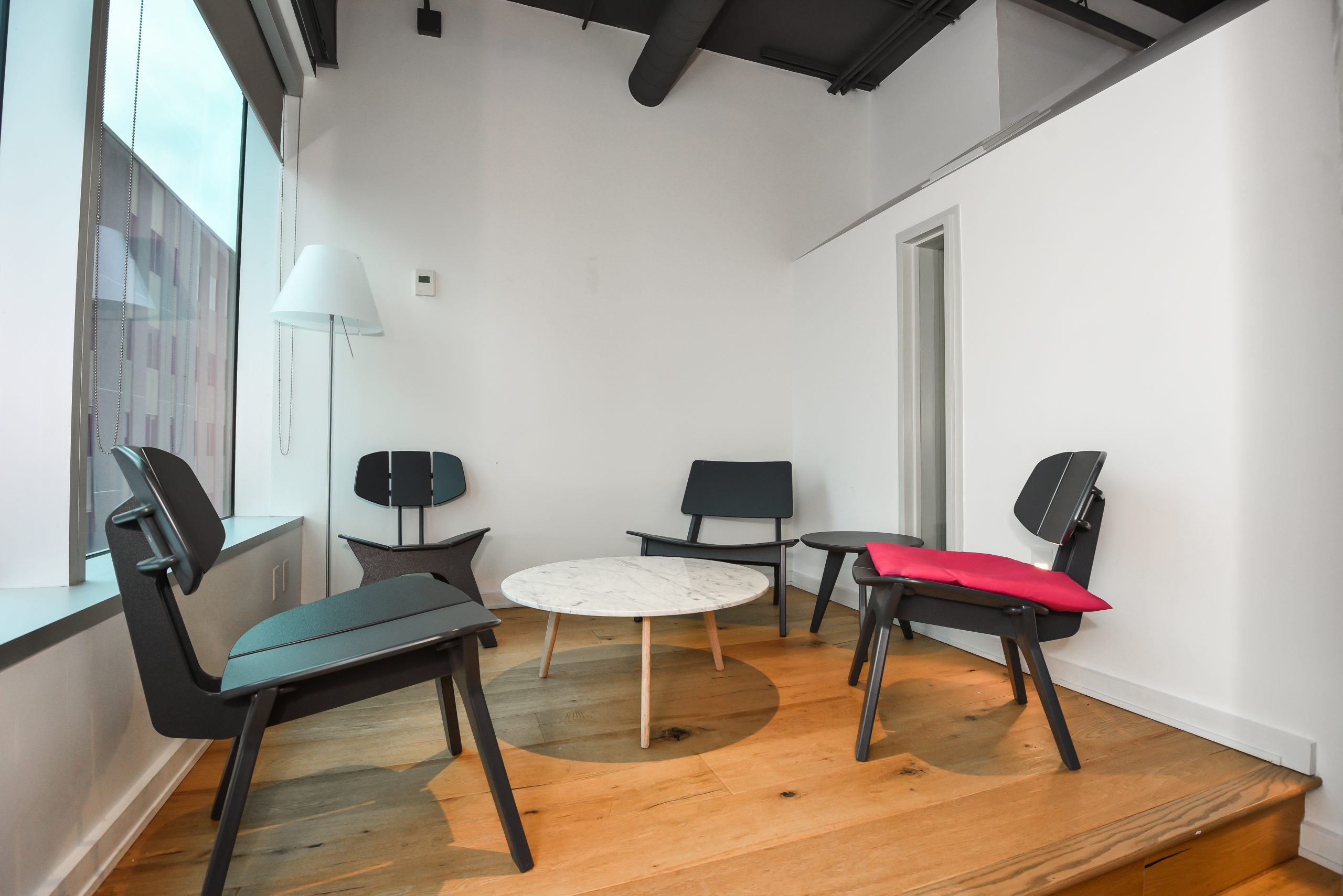 Small, modern office meeting nook with a round table and black chairs.