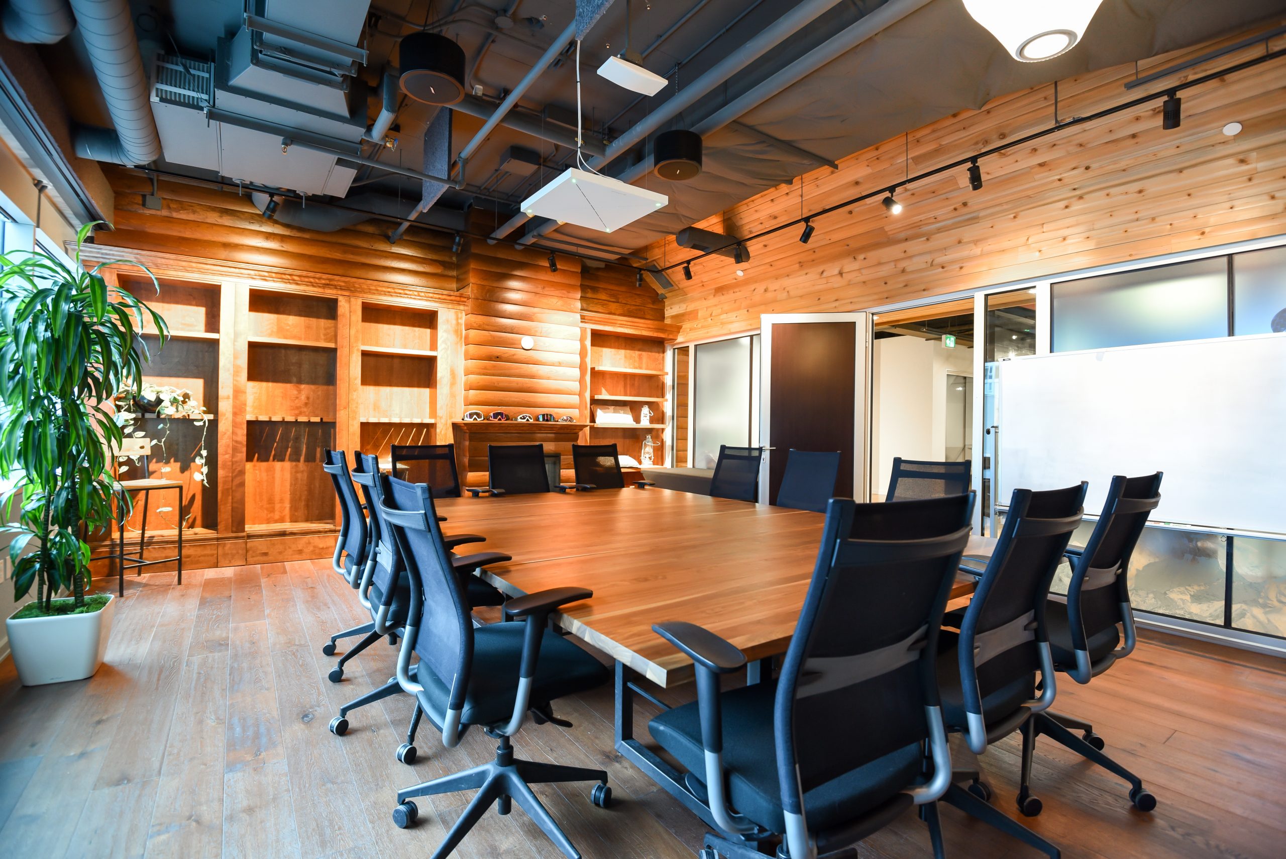 A meeting room with a large wooden table, black chairs, wooden walls, and exposed ceiling elements.