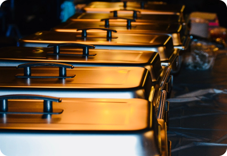 A row of covered chafing dishes on a buffet table.