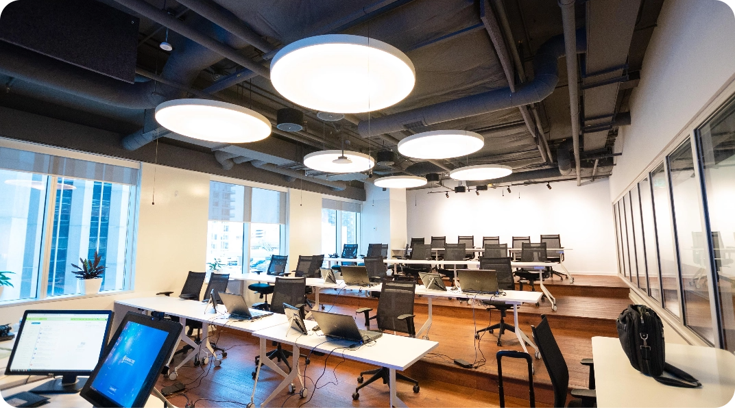 Modern office space with white desks, black chairs, and circular ceiling lights.