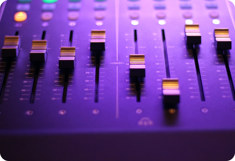 Audio mixing console with multiple faders and illuminated buttons.