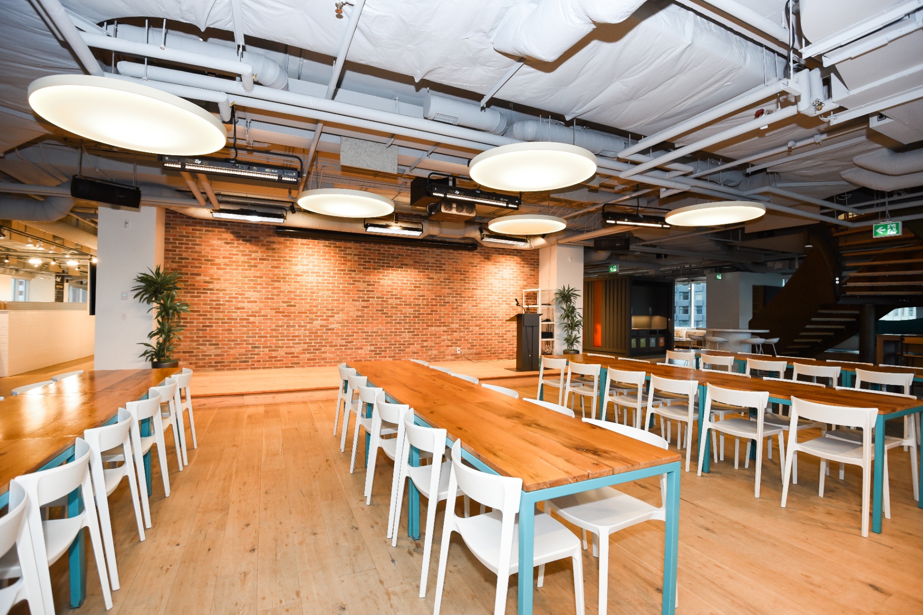 Event space with long tables, white chairs, a stage, and brick wall.