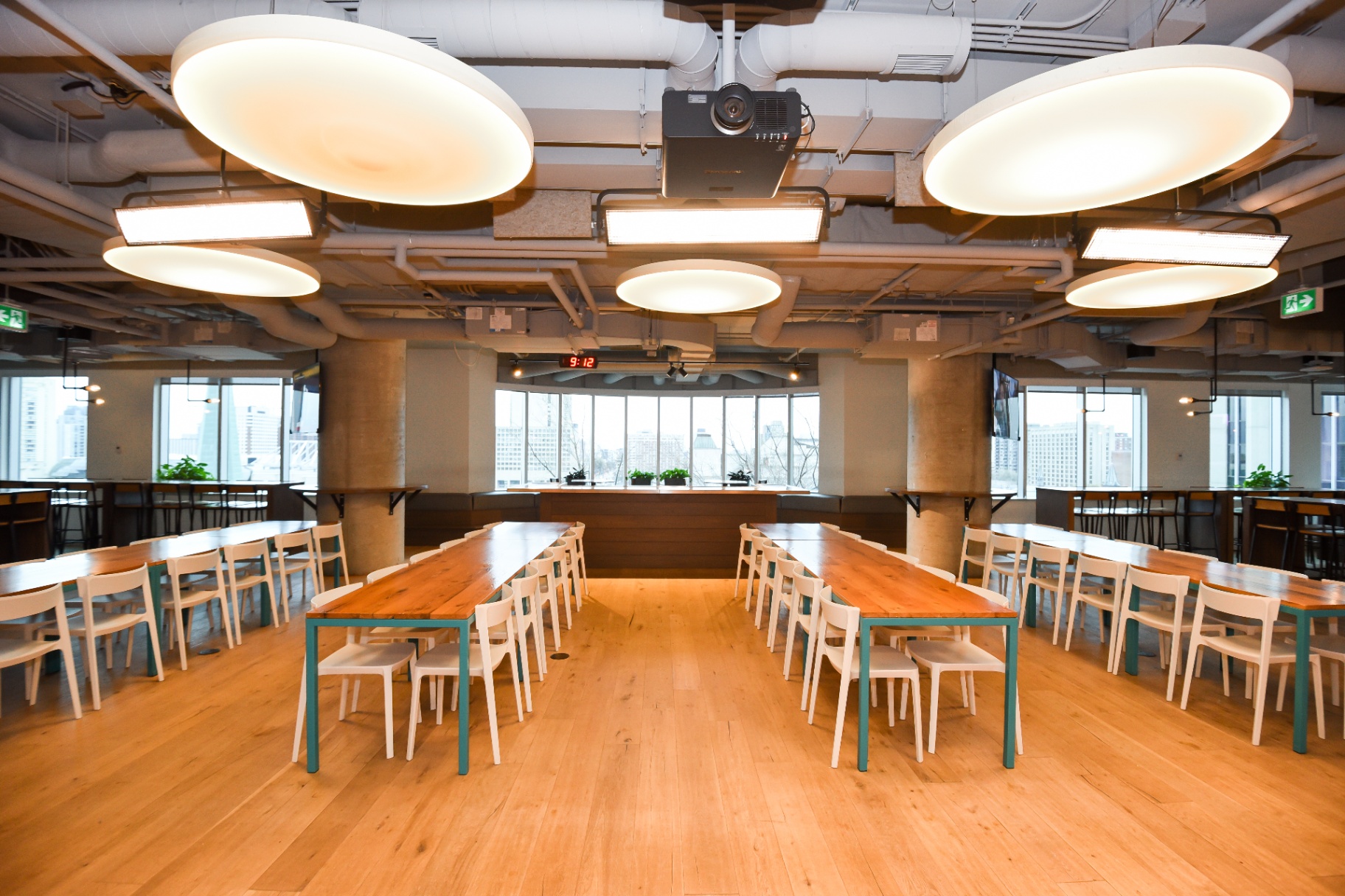 A well-lit, open event space with multiple long wooden tables and white chairs.