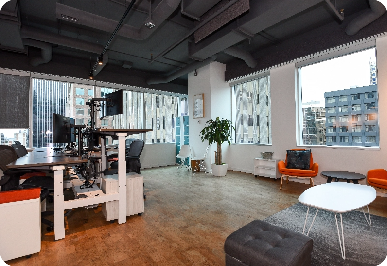 Modern office space with desks, computers, lounge area, and city views.