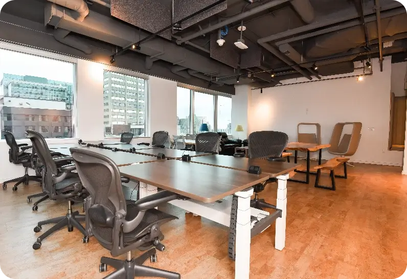 Premium office space with desks, chairs, and large windows showing city buildings.