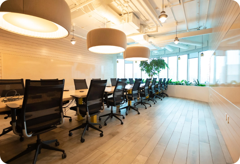 A bright and spacious conference room with a long table, black chairs, and large pendant lights.