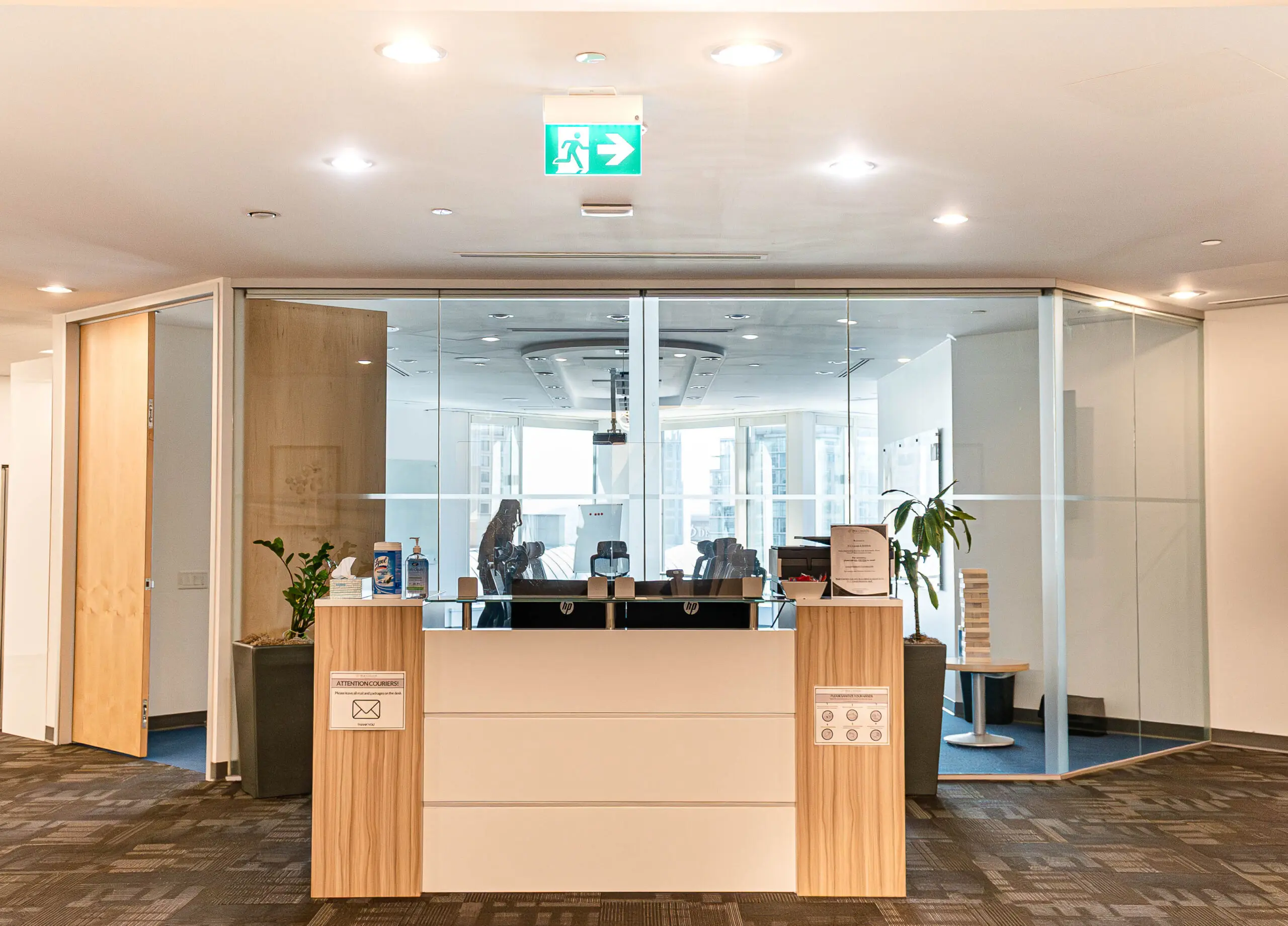 A modern office reception area with a white and wood desk facing a glass-enclosed conference room.