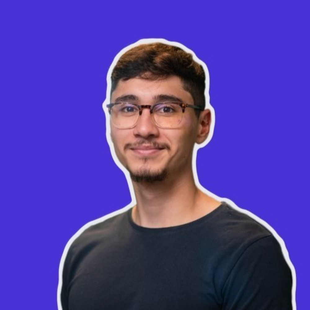 Portrait of a young man with glasses and a goatee against a purple background.