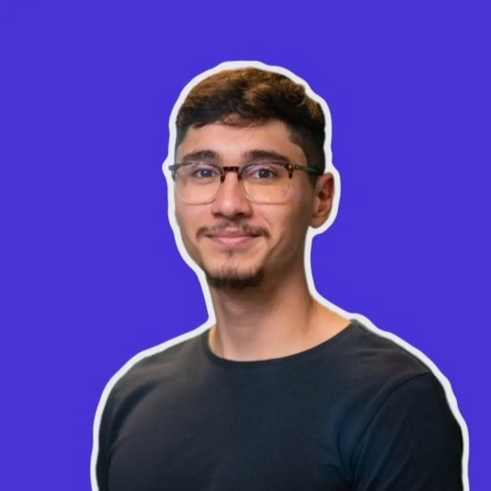 Portrait of a young man with glasses and a goatee against a purple background.