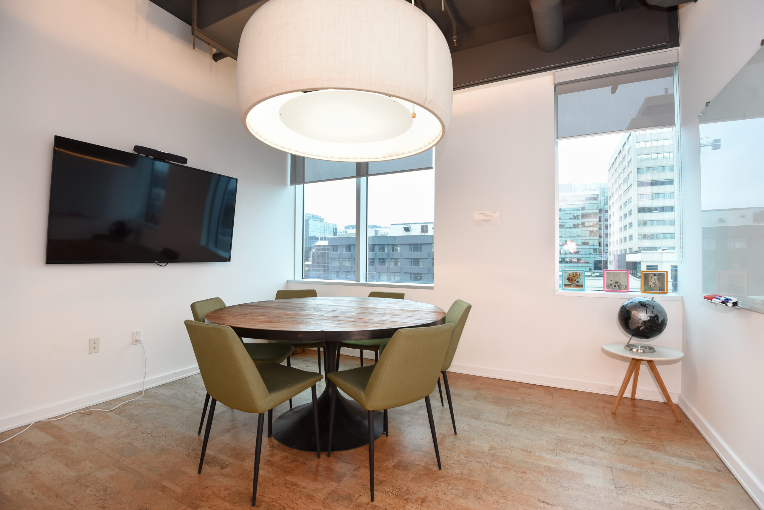 Small, modern meeting room with a round wooden table and olive-green chairs.