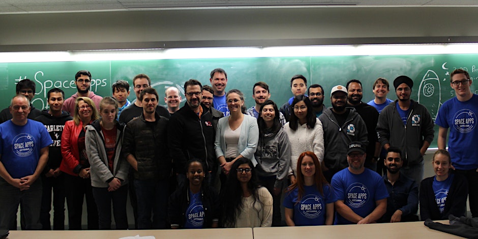 Group photo of about 25 people in front of a chalkboard with "Space Apps" written on it.