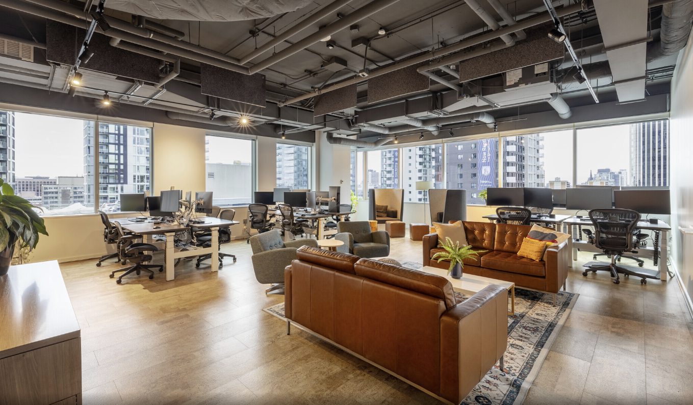 Modern office at TCC Canada with desks, computers, brown sofas, and city views.