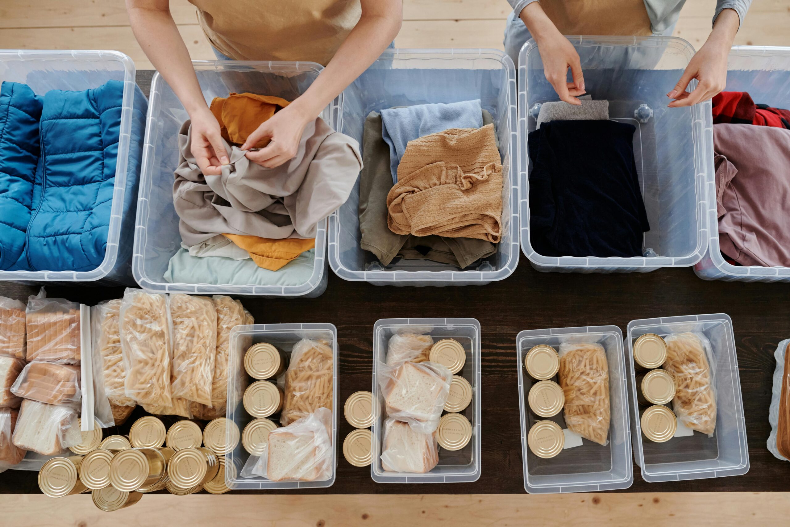 People sorting donated clothes and non-perishable food into clear plastic containers.