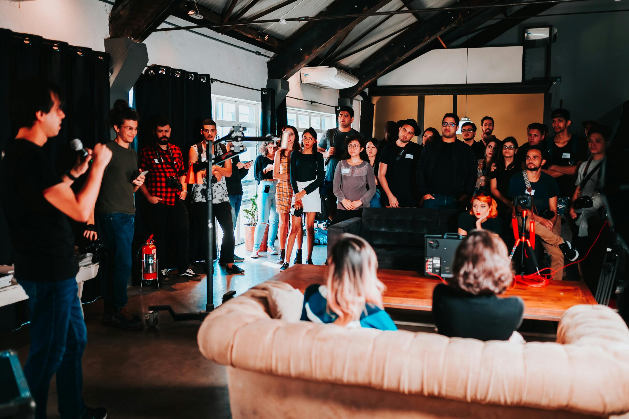 A group of people appear to be attending a casual event or presentation in a loft-style space.