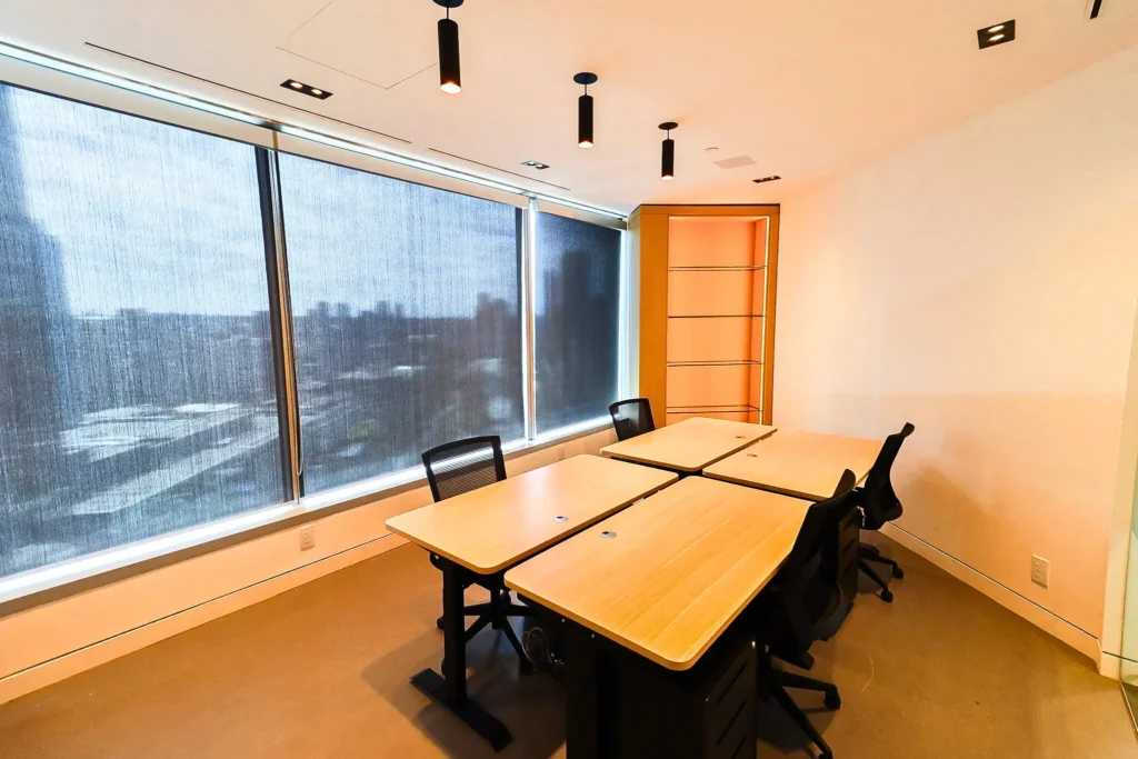 A contemporary office room with four desks, black chairs, and large windows with blinds. Found in TCC Canada-The City Centre, a new workspace in Vancouver