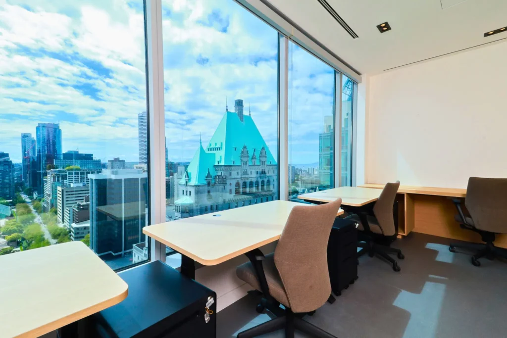 A bright office space at TCC Canada-The City Centre, with desks and chairs, featuring large windows overlooking a city skyline.