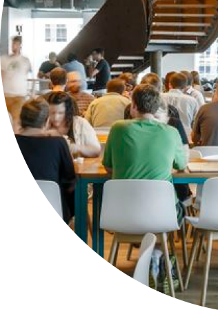 Coworking space with people collaborating at tables, featuring a modern and open environment with a staircase in the background.