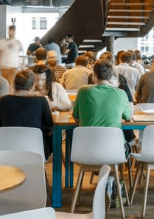 Coworking space with people collaborating at tables, featuring a modern and open environment with a staircase in the background.
